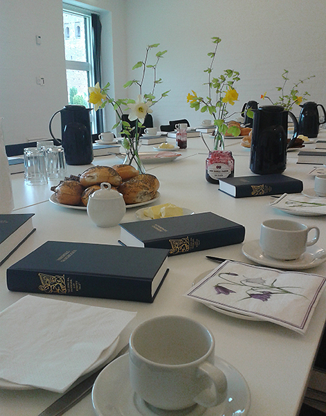 Billede af opdækket kaffebord, med blomster, sangbøger og rundstykker.